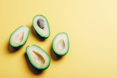 Halves of avocado on yellow background with sharp shadows. Healthy vegan food concept. Top view, copy space.
