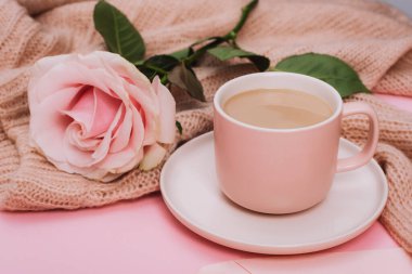 A coffee cup and pink rose on knitted sweater. Holiday concept. Closeup.