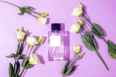 Purple perfume bottle and white eustoma flowers in sunlight. Top view, flat lay, mockup.