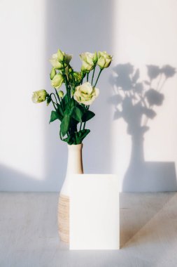 Bouquet of estouma flowers in vase and blank card on a table in sunlight. Mockup.