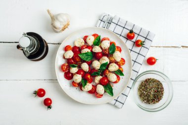 Italian caprese salad with cherry tomatoes, mozzarella, basil, garlic, balsamic sauce on a white wooden table. Top view, flat lay.