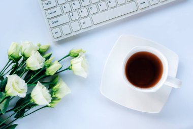 A cup of coffee, computer keyboard and eustoma white flowers on light blue background. Top view, flat lay.