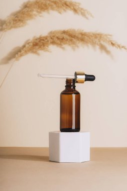 Brown cosmetic serum bottle on a podium and pampas grass on beige background. Natural skin care cosmetics concept. Closeup.