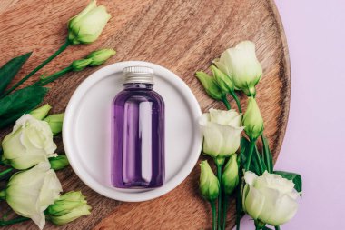 Mor kozmetik şişesi ve ahşap tepside beyaz Eustoma çiçekleri. Üst manzara, düz uzanma.