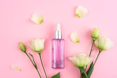 Mor kozmetik şişesi ve pembe arka planda beyaz Eustoma çiçekleri. Üst manzara, düz uzanma.