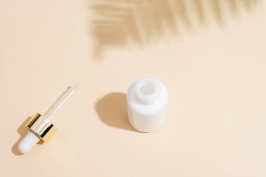 Pipetli beyaz damlacık şişesi ve bej arka planda eğreltiotu yaprağı gölgesi. Doğal yaşlanmayı önleyici kozmetik konsepti. Üst görünüm.