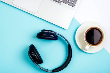 Ofis masası. Bilgisayarlı çalışma alanı, ofis malzemeleri, kulaklıklar ve mavi arka planda kahve fincanı. Üst manzara, düz uzanma.