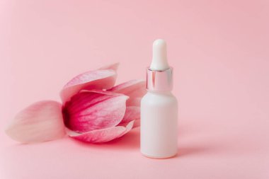 Pembe arka planda beyaz bir serum şişesi ve manolya çiçeği. Model yap, boşluğu kopyala.