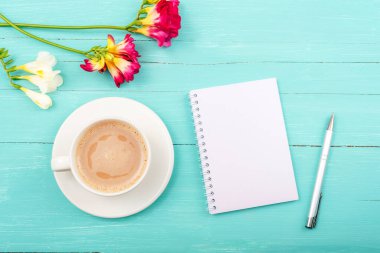 Blank notepad, pen and coffee cup on turquoise wooden table with freesia flowers. Top view, flat lay, mockup. clipart