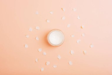 Kozmetik krem kavanozu ve mercan pembe arka planda beyaz çiçek yaprakları. Üst manzara, düz uzanma.