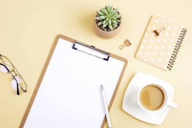 Boş dosya, not defteri, gözlük, kahve fincanı ve açık bej arkaplanda aksesuarları olan bir masaüstü. Üst görünüm, düz görünüm, model.