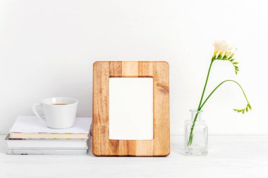 Sahte ahşap çerçeve, kitaplar, kahve fincanı ve beyaz masadaki vazodaki frezya çiçekleri. Boşluğu kopyala.