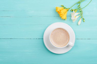 Kahve fincanı ve turkuaz mavi ahşap masada sarı frezya çiçekleri. Üst görünüm, düz görünüm, kopyalama alanı.