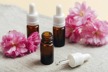 Temel yağlı kahverengi cam damlalar ve tekstil peçetesinde pembe kiraz çiçekleri. Aromaterapi, güzellik tedavi konsepti. Yakın çekim..