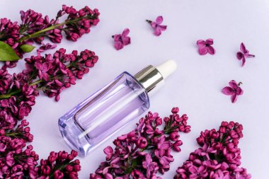 Açık mor arka planda serum şişesi ve leylak çiçekleri. Doğal kozmetik, cilt bakımı konsepti. Üst görünüm.