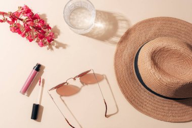 Tarafsız bir zeminde kadınların yaz aksesuarlarıyla yatıyordu. Güneş gözlüğü, hasır şapka, ruj ve kırmızı çiçek. Acımasız gölgeler. Üst görünüm.