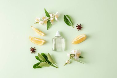 Parfüm şişesi ve limon meyvesi, yasemin çiçekleri, açık yeşil arka planda yıldız anason. Üst manzara, düz uzanma.