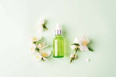 Yeşil kozmetik serumu şişesi ve beyaz yasemin çiçekleri. Doğal kozmetik, cilt bakımı konsepti. Üst manzara, düz uzanma.