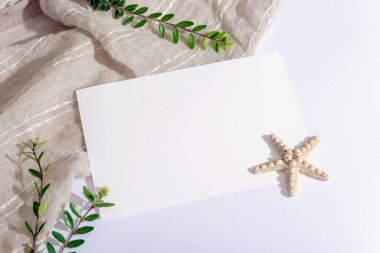 Boş kağıt çarşaf, denizyıldızı ve yeşil yapraklar beyaz masada. Üst görünüm, düz görünüm, model.