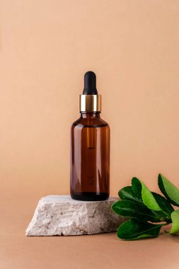 Doğal taş kürsüde kahverengi kozmetik serumu şişesi ve doğal bej arka planda yeşil yapraklar. Yakın çekim..