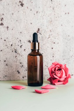 Kahverengi serum şişesi ve gül çiçeği doğal taştan arka planda. Yakın çekim..