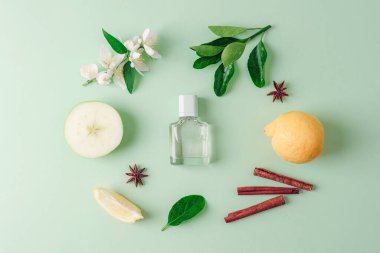 Parfüm şişesi ve elma, limon meyvesi, yasemin çiçekleri, açık yeşil arka planda yıldız anason ve tarçın çubukları. Üst manzara, düz uzanma.