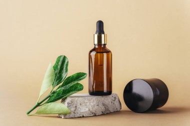 Doğal taş podyum ve krema kavanozunda kahverengi kozmetik serumu şişesi nötr bej arka planda yeşil yapraklar. Yakın çekim..