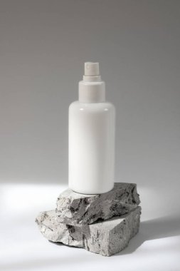 Beyaz kozmetik şişesi taş podyumda beyaz arka planda keskin gölgelerle. Yakın çekim..