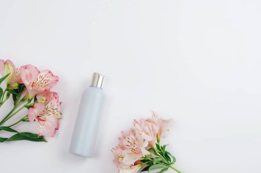 Mavi kozmetik şişesi ve beyaz arka planda Alstroemeria pembe çiçekleri, düz yatış, üst manzara. Damgalamak için boş etiket, maket. Doğal organik kozmetik ürünleri. Boşluğu kopyala.