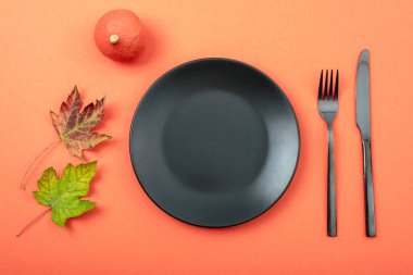 Turuncu zemin üzerinde boş siyah plaka ile sonbahar masa ayarları. Şükran Günü, Cadılar Bayramı süsü. Üst görünüm, düz görünüm, kopyalama alanı.