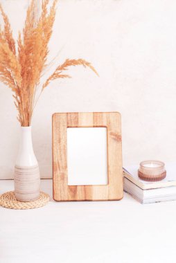 Sahte ahşap çerçeve, kitaplar, aroma mumu ve beyaz masadaki vazodaki otlar. Boşluğu kopyala.