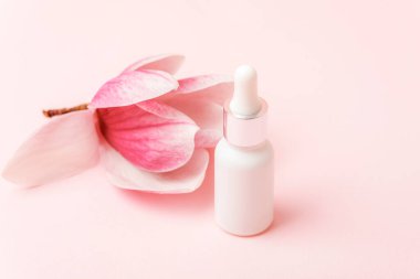 Kozmetik beyaz serum şişesi ve pembe arka planda manolya çiçeği. Mockup, boşluğu kopyala.