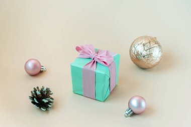 Pembe fiyonklu Teal mavisi hediye kutusu, Noel topları ve bej arka planda çam kozalağı.