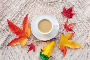 Kahve fincanı, sarı balkabağı ve sonbahar yaprakları pembe örülmüş süveter, üst manzara. Sonbahar kavramı.
