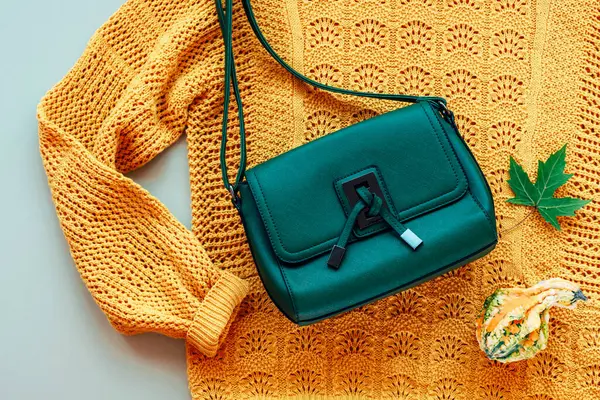 Flat lay of woman\'s yellow sweater and green bag with small pumpkin and autumn leaf on light green background. Autumn fashion concept. Top view, flat lay.