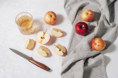 Taze olgun elmalar ve bir bardak elma suyu ya da elma suyu ya da beyaz masanın üzerinde gri peçete ve bıçakla sirke. Sonbahar hasadı, Şükran Günü konsepti. Üst manzara, düz uzanma.