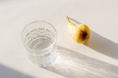 Güneş ışığında su ve beyaz masada armut meyvesi olan bir bardak. Durgun hayat. Üst görünüm.