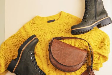 Sarı süveter ve kahverengi çantanın düz yatışı, tarafsız bej arka planda bir çift bot. Sonbahar moda konsepti. Üst manzara, düz uzanma.
