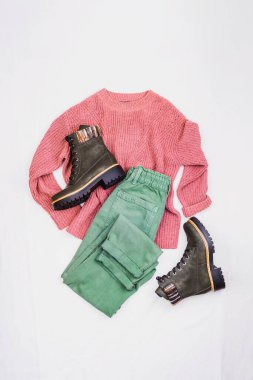 Mor kazak, yeşil kot pantolon ve botlar. Hafif arka planda rahat kadın kıyafetleri. Üst manzara, düz uzanma.