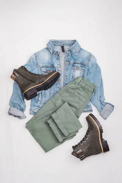 Blue jeans jacket, green jeans and boots. Comfortable casual women's clothing on a light background. Top view, flat lay.