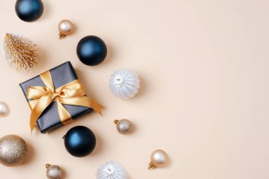 Altın kurdeleli siyah hediye kutusu ve bej arka planda Noel mücevherleri. Üst görünüm, düz görünüm, kopyalama alanı.