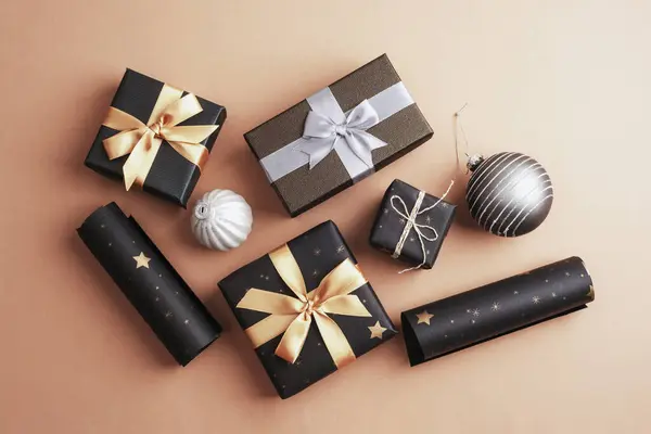 Christmas gifts in black boxes with golden and silver bows on beige background. Top view, flat lay.