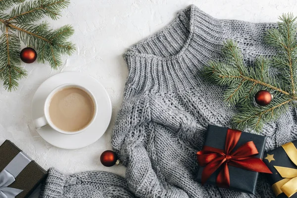 A cup of coffee and Christmas gifts on grey sweater on white background. Top view, flat lay.