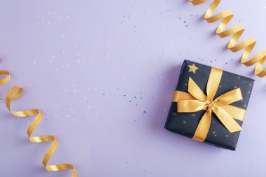 Mor arka planda konfetiyle birlikte hediye kutusu ve altın süsleme. Noel, yeni yıl ya da doğum günü konsepti. Üst görünüm, düz görünüm, kopyalama alanı.