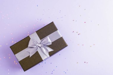 Mor arka planda konfetili bir kutuda hediye. Noel ya da doğum günü, tatil konsepti. Üst görünüm, düz görünüm, kopyalama alanı.