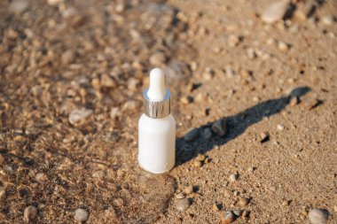 Hyaluronik asit, kum plajı arka planında beyaz bir şişe serum. Peptit ve kolajenle serum ürünü kozmetik. Modern marka kozmetik ambalajı. Üst görünüm.