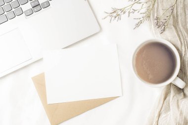 Kahve fincanı, dizüstü bilgisayar, içinde boş kart olan zarf ve beyaz çarşaflarda kurumuş çiçekler. Rahat bir iş yeri, konfor, kızlık zarı konsepti. Üst görünüm, düz görünüm, model.
