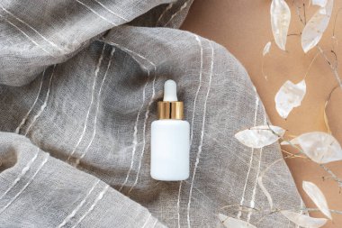 Beyaz serum şişesi, bej kumaşlı ve ay çiçekli. Doğal kozmetik konsepti. Üst manzara, düz uzanma.
