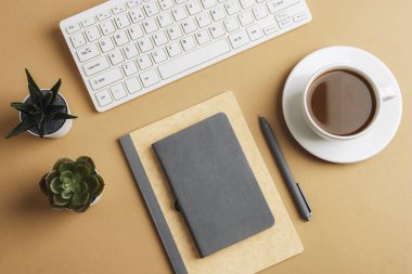 Not defteri, klavye, kahve fincanı ve bej masadaki sulu bitkiler. Üst manzara, düz uzanma.