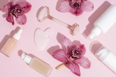Yüz estetik silindiri ve pembe orkide çiçekleri ve serum şişeleriyle gua sha kazıyıcı. Keskin gölgeler. Ev spa konsepti. Üst manzara, düz uzanma.